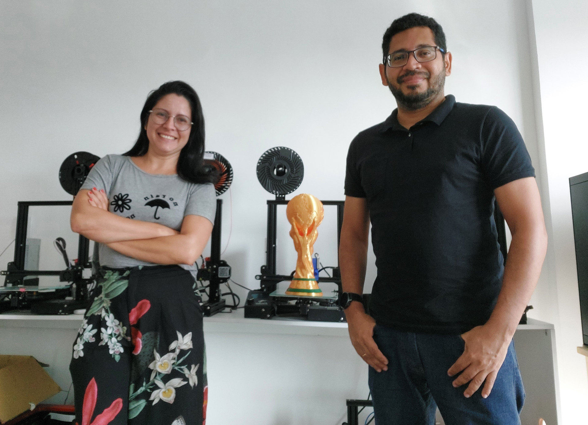 Walquiria Mélo e Thiago de Moraes, fundadores da Tudo 3D, em frente às impressoras 3D com o troféu da Copa do Mundo impresso